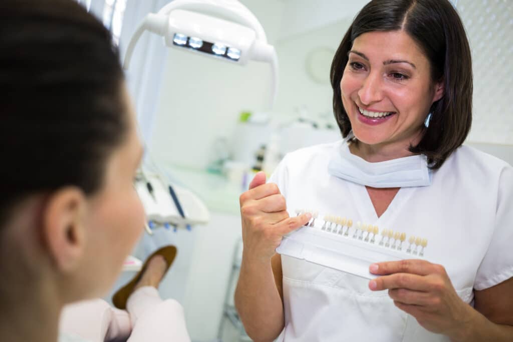 Dentist examining patient with dental veneer shade guide